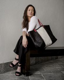 Female model sitting on wooden bench in dramatic lighting wearing white sweater and black pants with black strappy heels and large handbag