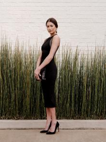 Female model standing in front of green horse hair against white brick wearing Narciso Rodriguez Gianvito Rossi shoes, Rene Escobar earrings, and B May clutch