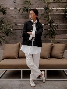 Female model standing in front of outdoor furniture in front of a wood wall and bamboo wearing white Jil Sander outfit with Maison Margiela sneakers