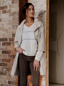 Female model standing in by brick wall wearing trench coast, sweater, and pants by Peserico