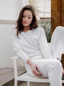 Female model sitting in chair in front of a fountain wearing a white Brunello Cucinelli sweater & white Ql2 pant.