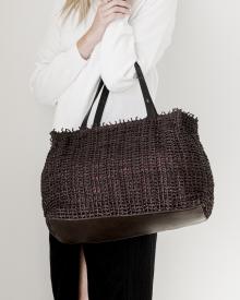 Female model against white background in white sweater and black jeans wearing brown threaded Henry Beguelin handbag