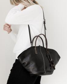 Female model against white background in white sweater and black jeans wearing black leather Henry Beguelin handbag