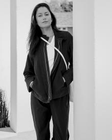 Black and white photo of female model leaning against white corner wall wearing a Labo.art Jacket, Frame Tee, and  Aspesi Pant