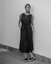Black and white photo of female model leaning against white wall wearing a Peserico Dress and The Row Sandal 