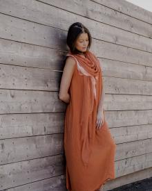 Female model leaning against wooden wall in dramatic lighting wearing orange Minina Dress