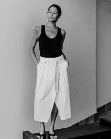 Black and white photo of female model against white wall wearing a black Christina Lehr Tank and a black Transit Skirt 
