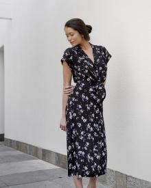 Female model standing in front of white wall in dramatic lighting wearing a blue Veronica Beard Dress with flower detail prints