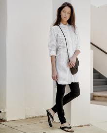 Female model standing near white wall with handbag wearing long Nili Lotan Shirt and Annette Gortz Legging