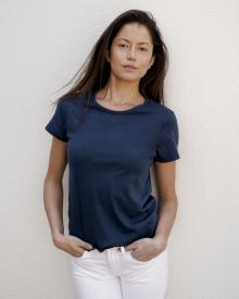 Female model leaning against white wall wearing navy blue Christina Lehr Tee and white Frame Jean 