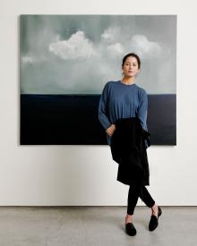 Model standing in front of painting wearing blue 6397 Sweater & Jeans and black MaxMara Trench Coat
