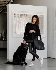 Model standing in art gallery with black dog wearing black Varley Sweatshirt, black Frame Jean, white Golden Goose Sneaker, and black Amiacalva Tote