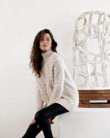 Model leaning back on white cube wearing off white Vince Cable Turtleneck Sweater and black Frame Leather Jean