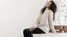 Model leaning back on white cube wearing off white Vince Cable Turtleneck Sweater and black Frame Leather Jean