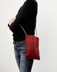 Woman wearing black sweater and blue jeans holding red Amiacalva Pouchette crossbody