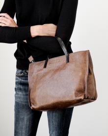 Woman wearing black sweater and blue jeans holding brown B. May bag