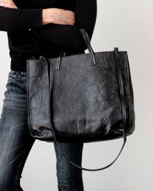 Woman wearing black sweater and blue jeans holding black B. May bag